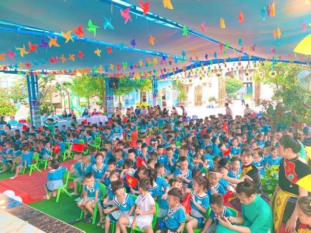 A group of children sitting on green chairs under a canopy

Description automatically generated